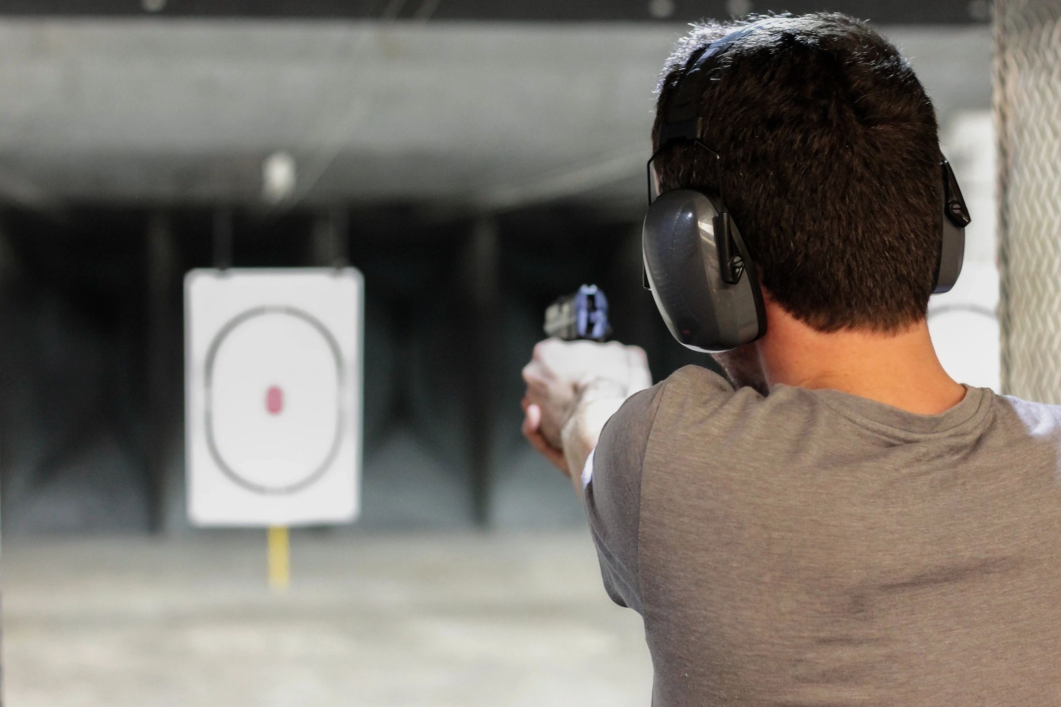 Back of man aiming pistol downrange at target