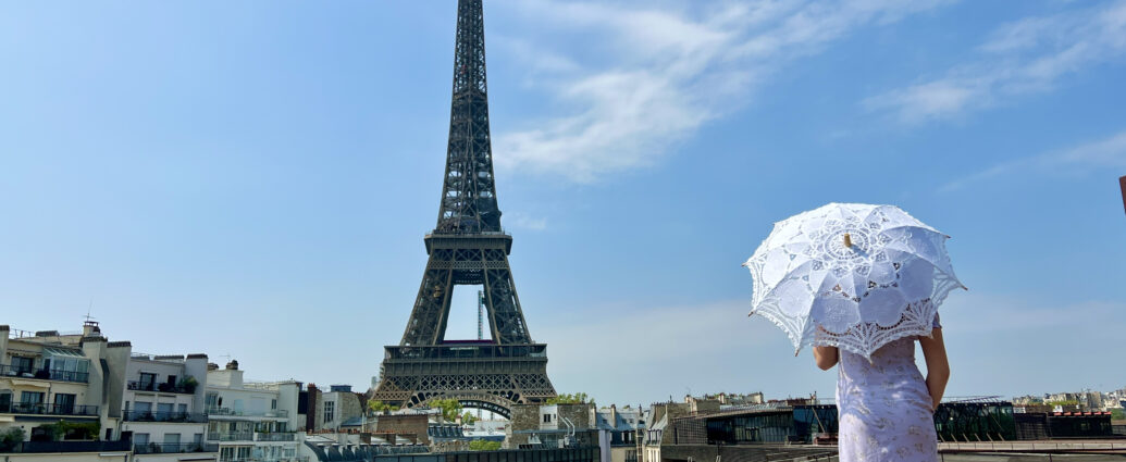 a beautiful yaoung girl in a summer dress stands against the backdrop of the Eiffel Tower with a lace umbrella