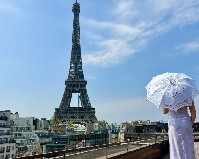 a beautiful yaoung girl in a summer dress stands against the backdrop of the Eiffel Tower with a lace umbrella